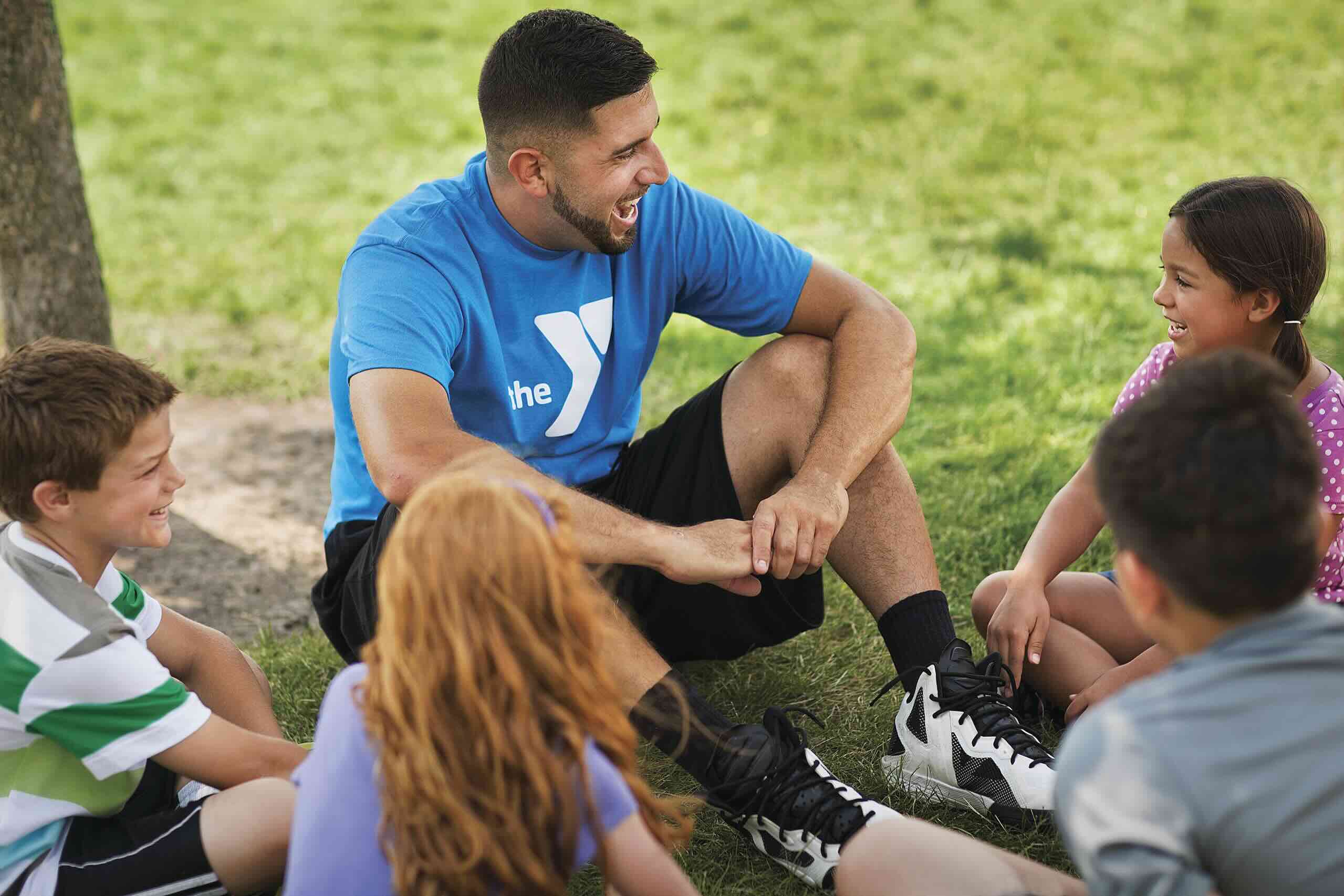 A small group of children sitting in a circle around a Y staff member enjoying the outdoors.