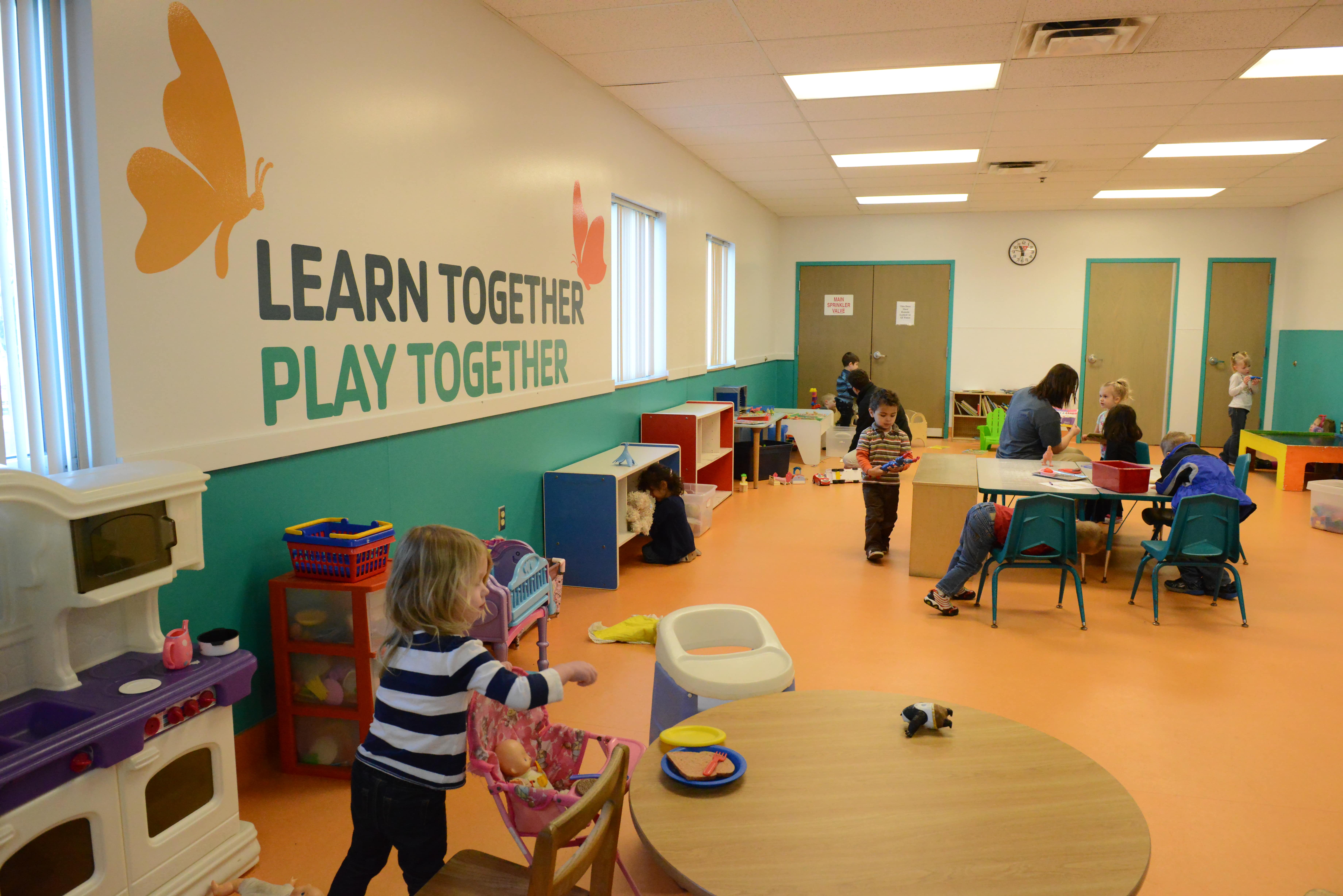 Photo of Kids Zone area that shows young children playing and the words "Learn Together. Play Together" in large letters on the wall, along with graphics of two butterflies.