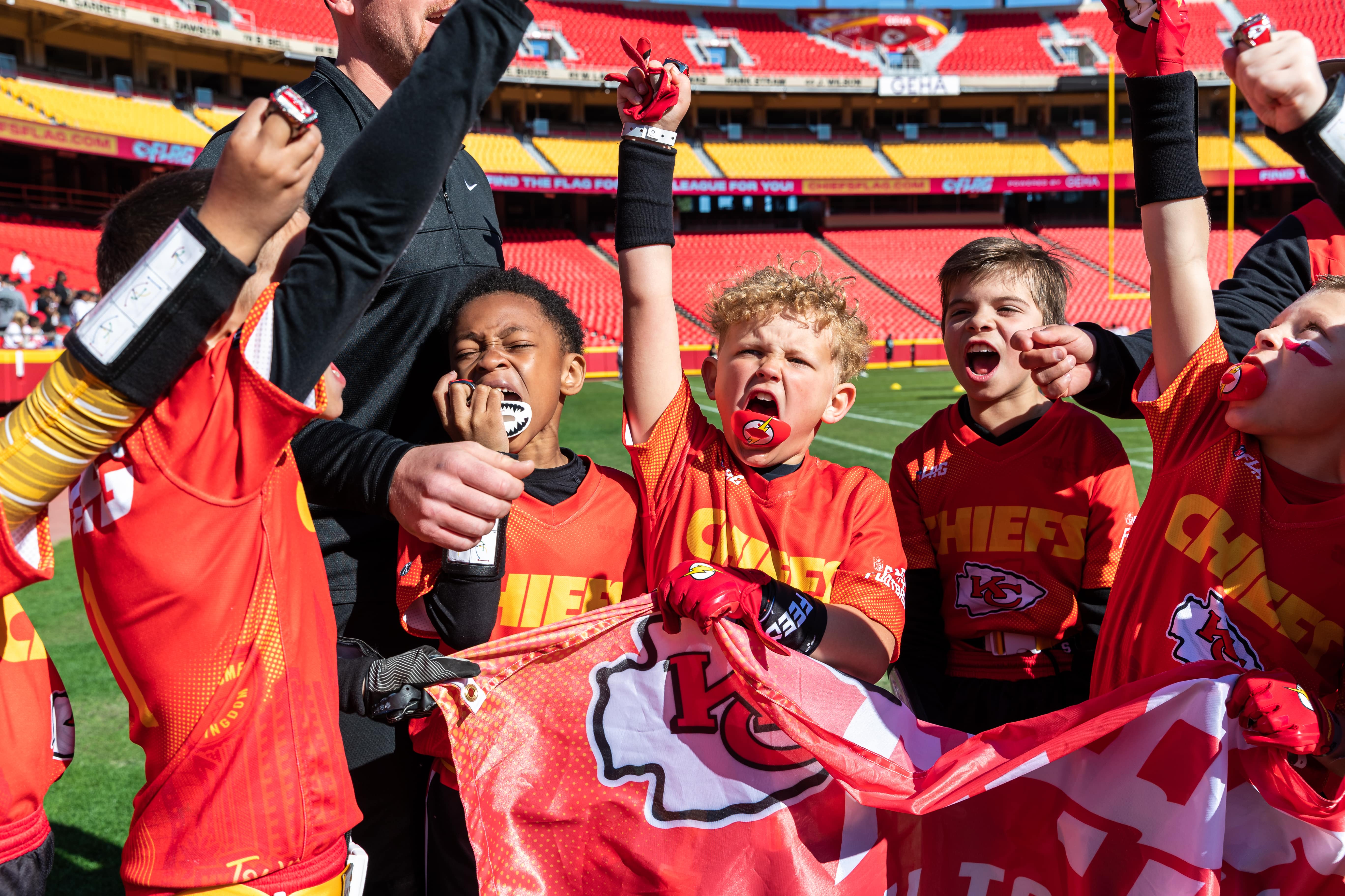 Five boys in YMCA Chiefs Flag Football uniforms cheering with arms in the air