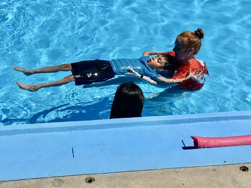 YMCA instructors helps a student float on their back during a swim lesson as part of the inaugural Learn to Swim program with GEHA in summer 2022.